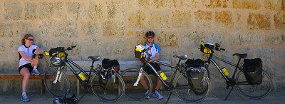 Friends rest by their touring bicycles at an old Romanesque church along the Camino de Santiago