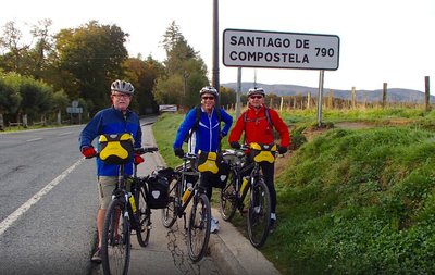Group of friends pose by their touring bicycles at the sign for Santiago de Compostela at Roncesvalles