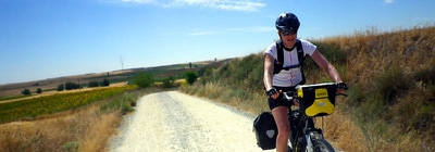 Lone female bicycle traveler rides on a gravel road along the Camino de Santiago